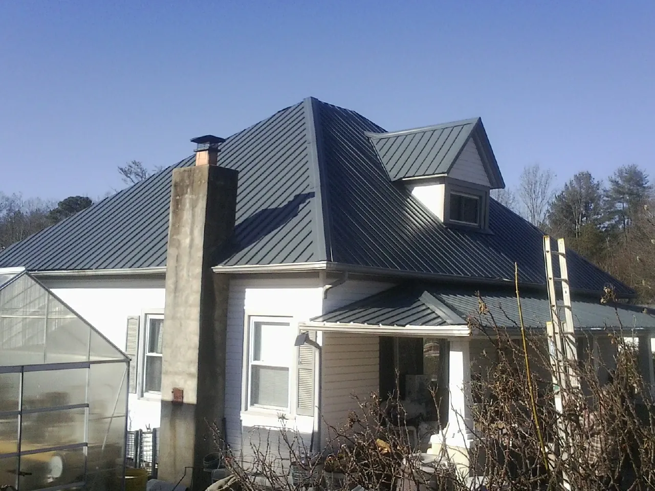 Dark blue standing seam metal roof on a white farmhouse with dormer — Slate & Tile Roof Repair by Roofing Brothers in East Calais