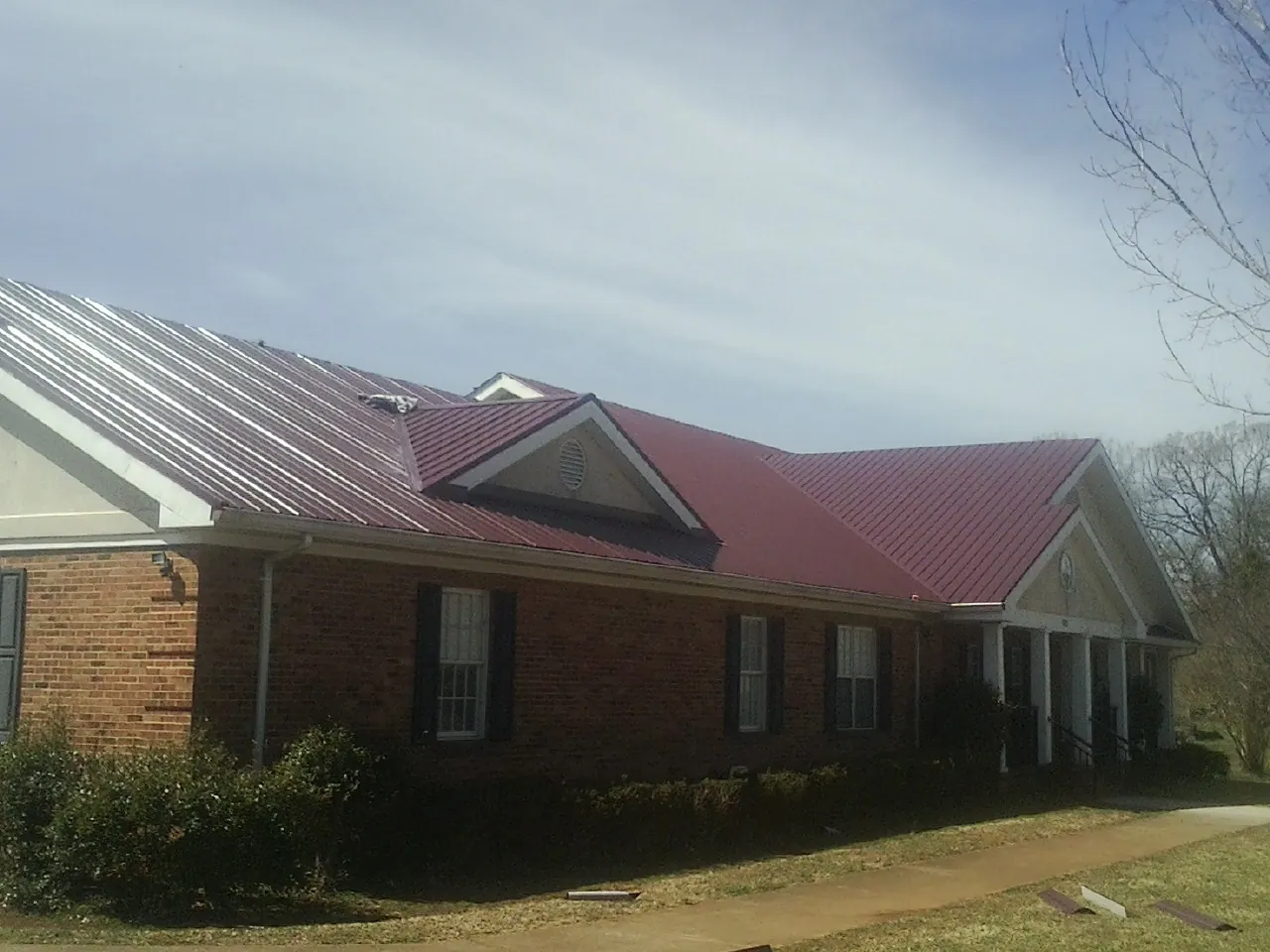 Red metal roof with gabled entries on a long brick building, from a Hail Damage Roof Repair job in East Calais