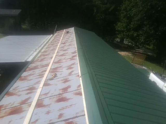 Old rusted panels beside newly installed green metal roofing — Wind Damage Roof Repair by Roofing Brothers in East Calais