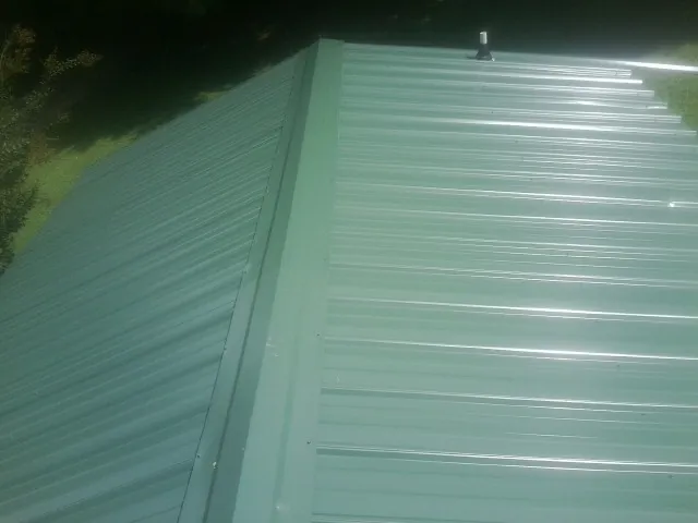 New green metal panels meeting at the ridge of a roof — Flat Roof Repair work by our crew in East Calais