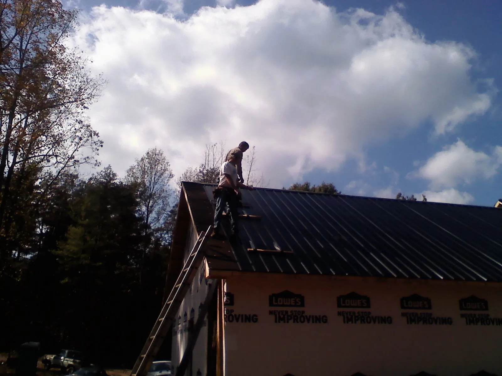 Roofer fastening dark metal panels high against a cloudy sky, from a Roof Inspection job in East Calais
