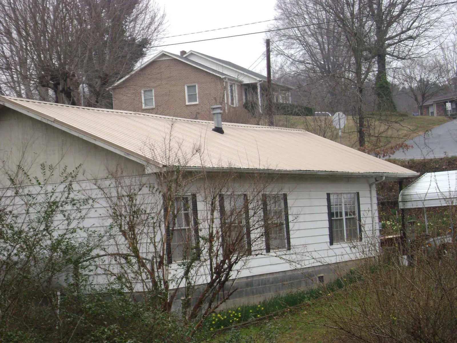 Tan metal roof on a white sided house set into a hillside — Commercial Roofing by Roofing Brothers in East Calais