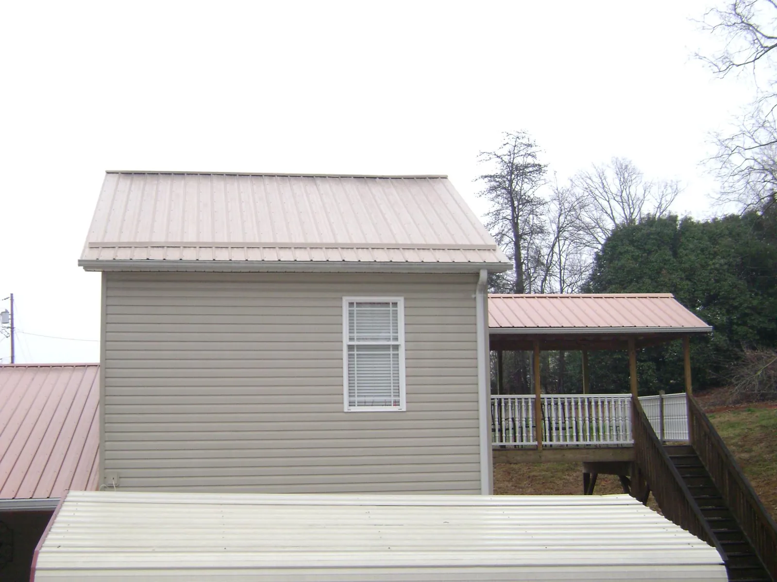 Tan metal roofs on a two story addition and attached porch, from a Roof Replacement job in East Calais